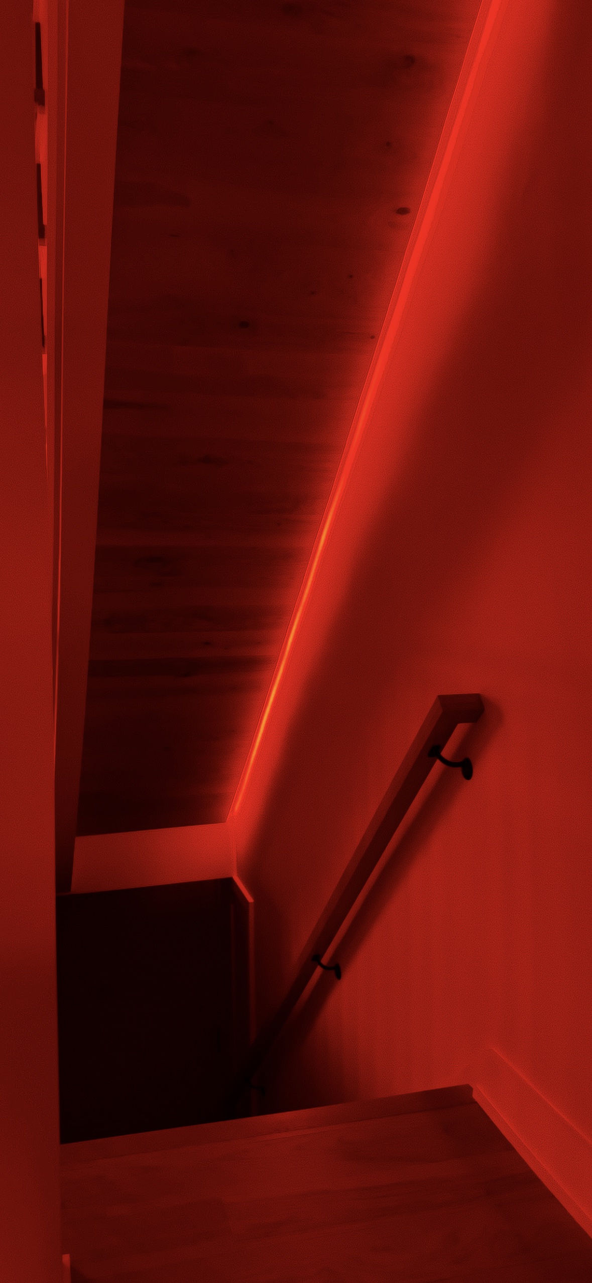 A stairwell at night — a single line of red light raking down warm wood
